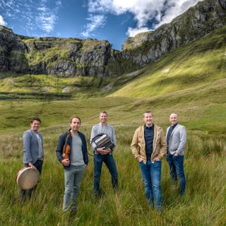 five men stand in a hilly field surrounding by cliffs